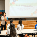 Lt. Gov. Luke speaking to middle school students with a presentation that reads ʻAct with Alohaʻ in the background.
